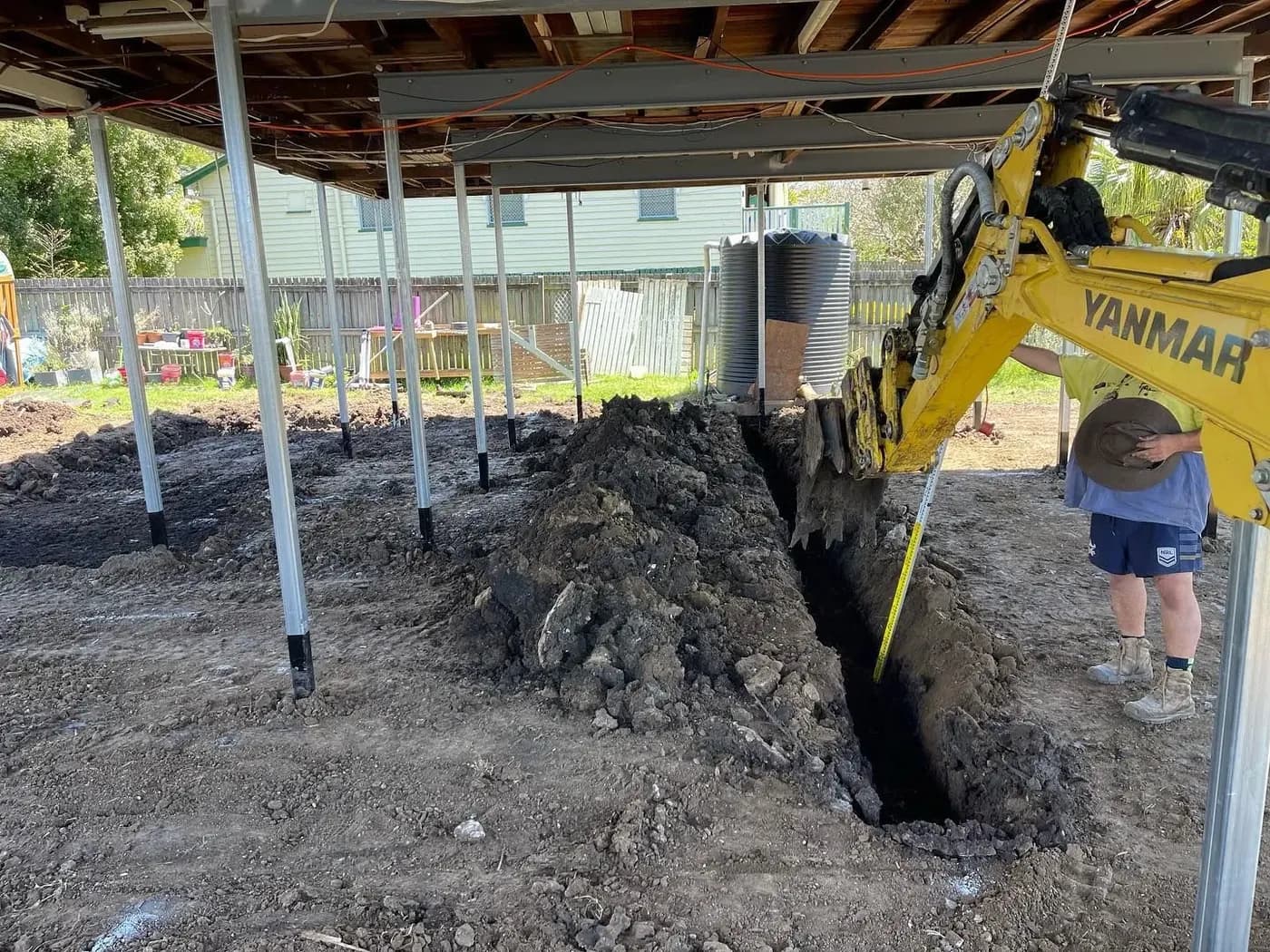 Excavator digging footing trenches beneath a raised home